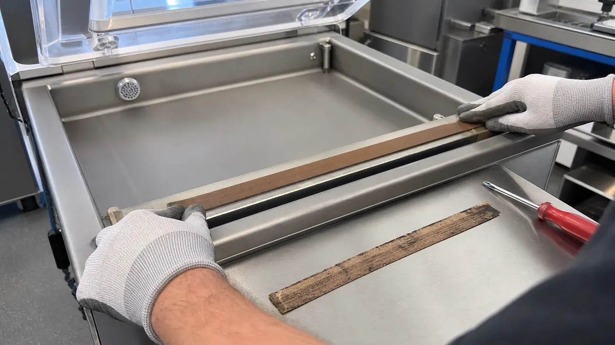 Maintenance technician smoothing brown PTFE-coated fiberglass tape over a vacuum packaging machine sealing bar